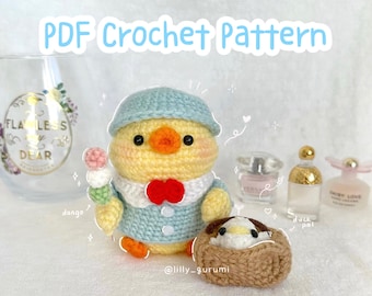 May include: A crochet pattern for a yellow chick wearing a blue hat and holding a dango. The chick is sitting next to a brown crocheted nest with a smaller chick inside. The pattern is available as a PDF download.
