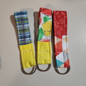 May include: Three fabric keychains with yellow, red, and blue fabric. Each keychain has a silver metal ring.