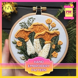 Peut inclure: Un motif de broderie à la main représentant un groupe de trois champignons aux chapeaux orange et aux pieds blancs, entourés de feuilles vertes et de fleurs jaunes. Le motif est présenté dans un cerceau de broderie en bois. Le texte "HAND EMBROIDERY PATTERN" est affiché sous le cerceau.