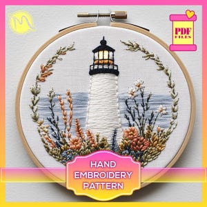 May include: Hand embroidery pattern featuring a white lighthouse with a yellow window, surrounded by a wreath of green and brown leaves and flowers. The pattern is in a wooden embroidery hoop.