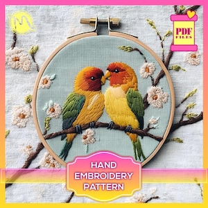 Op de afbeelding: Handborduurpatroon met twee tortelduifjes die op een tak zitten met delicate witte bloemen. Het patroon wordt getoond in een houten borduurring.