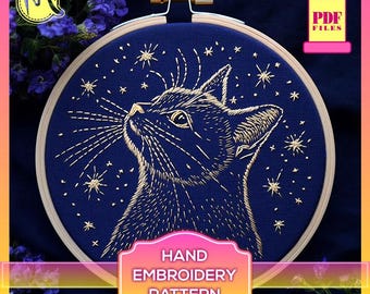May include: A hand embroidery pattern featuring a cat looking up at a starry night sky. The cat is outlined in gold thread on a dark blue fabric. The pattern is available as a PDF download.