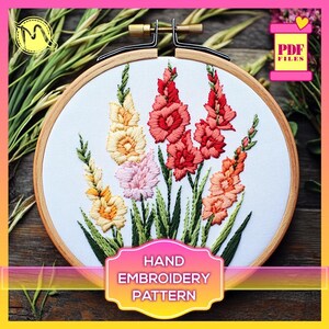 May include: Embroidered floral hoop art featuring a bouquet of pink, yellow, and red gladiolus flowers with green leaves. The hoop is made of wood and has a white fabric background. The text "HAND EMBROIDERY PATTERN" is printed on a label below the hoop.