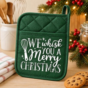 May include: A dark green quilted pot holder featuring a white graphic of a whisk and the text "WE whisk YOU A Merry CHRISTMAS". The square kitchen accessory has a top loop for hanging and a pocket design on the front for functional use.
