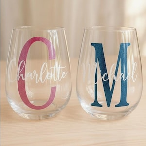 Könnte beinhalten: Zwei klare, stielose Weingläser mit personalisiertem Text. Ein Glas zeigt ein rosa glitzerndes "C" mit dem Namen "Charlotte" in weißer Schrift. Das andere Glas hat ein blau glitzerndes "M" mit dem Namen "Michael" in weißer Schrift.