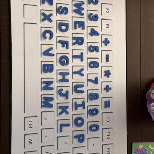May include: A white keyboard-shaped learning toy with blue magnetic letters and numbers. The letters and numbers are arranged on the keyboard layout. The toy includes function keys and control keys.