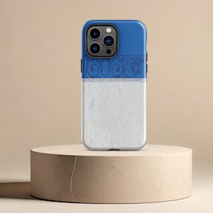 May include: A white and blue phone case with a decorative pattern. The case has a textured white bottom and a blue top with a floral design. The phone case is on a light brown pedestal.