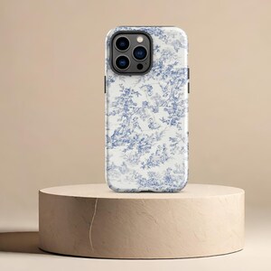May include: A white phone case with a blue and white floral pattern. The case has a black camera bump with four lenses.