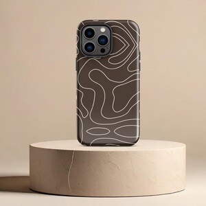 May include: A brown phone case with a white abstract pattern. The case has a black camera bump with three lenses.