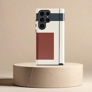 May include: A white phone case with a geometric design featuring black and white stripes and a red square. The phone case is on a beige pedestal.