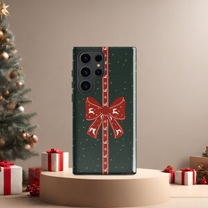 May include: A green phone case with a red bow and white reindeer print. The case has a textured background and a white border.
