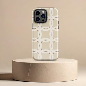 May include: A beige phone case with a white geometric pattern. The case is designed for an iPhone with a camera bump and a black border.