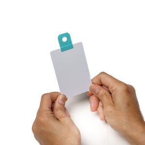 May include: A white card with a blue tab at the top is being held by two hands. The card is blank.