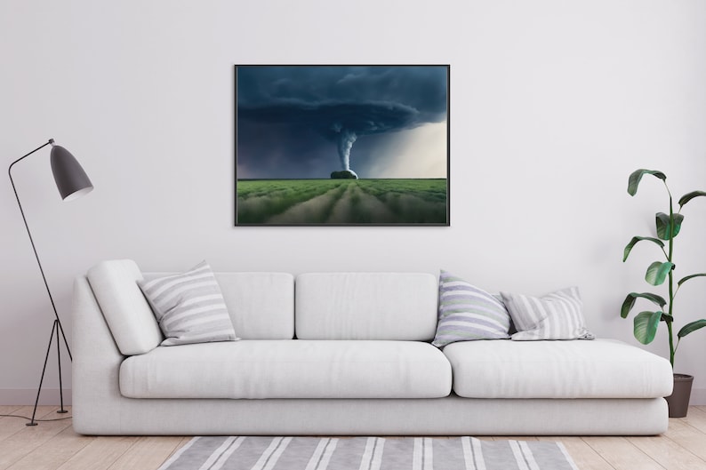 May include: A black and white photograph of a tornado in a field. The tornado is in the center of the image and is surrounded by a dark, stormy sky. The field is green and there are some trees in the distance.