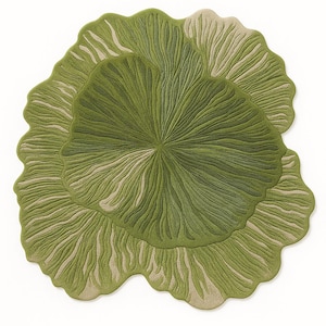 Puede incluir: Una alfombra verde con un diseño de hoja. La alfombra presenta una zona central verde oscuro rodeada por un borde verde claro y beige. El diseño tiene una apariencia texturizada y acanalada, que se asemeja a una gran hoja de planta.