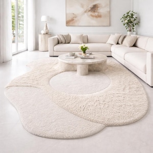 Peut inclure: Un tapis de sol crème de forme abstraite avec une surface moelleuse et texturée. Le tapis est placé dans un salon moderne, complétant le schéma de couleurs neutres des meubles et de la décoration. Le design du tapis ajoute un élément doux et organique à l'espace.