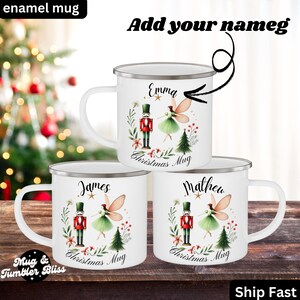 May include: White enamel mugs with silver rims, featuring personalized names and Christmas-themed designs. Each mug showcases a nutcracker, a fairy, and a Christmas tree. The mugs are labeled "Christmas Mug" and "Mug & Tumbler Bliss."