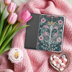 Könnte beinhalten: Transparente Hülle für einen E-Reader mit floralem und Schwert-Design. Die Hülle liegt auf einer rosa Strickdecke, neben rosa Tulpen und einer herzförmigen Schale mit Marshmallows. Ein Logo mit einer Biene ist ebenfalls sichtbar.