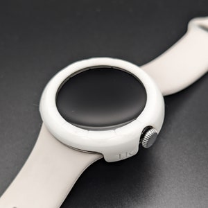 May include: White smartwatch with a round face and a white silicone band. The watch face is black and has a silver knob on the side.