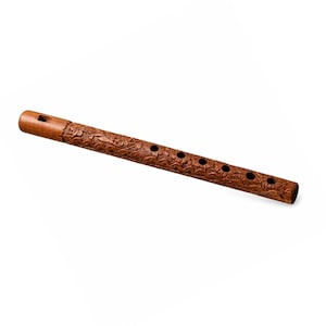 May include: A brown wooden flute featuring intricate floral carvings along its cylindrical body. The instrument includes a rectangular mouthpiece at one end and six circular finger holes arranged in a linear row along the top surface.