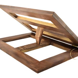 May include: A wooden book stand with a dark brown finish. The stand is open and has a hinged top. The stand is made of solid wood and has a simple design.