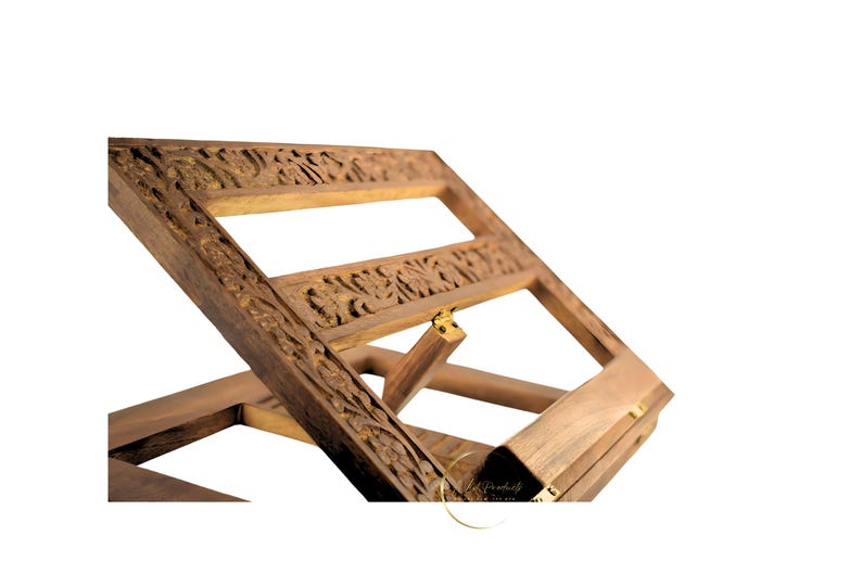 May include: A wooden book stand with intricate carvings and a brass hinge. The stand is made of dark brown wood and has a rectangular shape. It is designed to hold a book or other reading material at an angle.