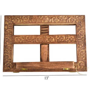 May include: A wooden book stand with intricate floral carvings. It measures 13 inches wide and 9 inches tall.