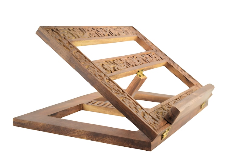 May include: A wooden book stand with intricate carvings. The stand is made of dark brown wood and has a hinged design that allows it to be folded flat for storage.