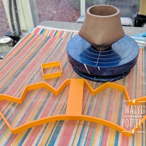 May include: A brown ceramic vase sits on a blue pottery wheel. An orange crown-shaped cutter and a square cutter are on a striped surface. The image includes the text "Waiyi Pottery".