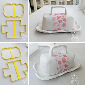 May include: White ceramic butter dish with a handle and a strawberry pattern. The dish sits on a matching scalloped base. Two yellow cookie cutters are also in the image.