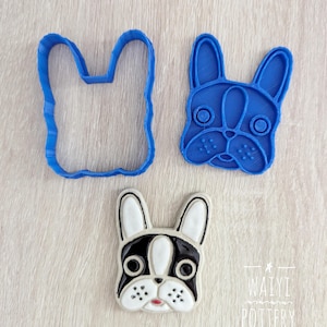 May include: Three French bulldog-themed items. A blue plastic cookie cutter in the shape of a French bulldog head, a blue plastic cookie cutter in the shape of a French bulldog head, and a ceramic French bulldog head with black, white, and pink details.