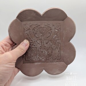 Pu&ograve; includere: Un sottobicchiere in ceramica marrone fatto a mano con un motivo floreale al centro. Il sottobicchiere ha una forma unica a quattro lobi. L'immagine include anche il testo "WAIYI POTTERY".