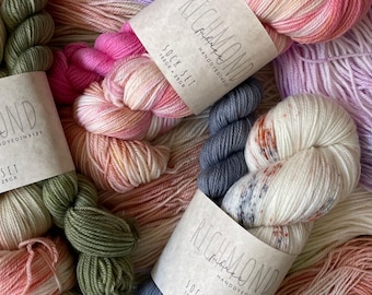 May include: Three skeins of hand-dyed yarn labeled Richmond Fibres Sock Set 100g-20g. The yarn features variegated colorways including olive green, soft pink, coral, lavender, and cream with dark speckles, arranged in a layered, textured display.