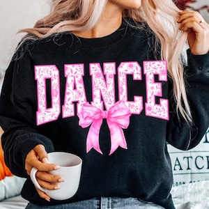 May include: Black sweatshirt with the word "DANCE" in pink letters with a floral pattern. A pink bow is centred below the word.
