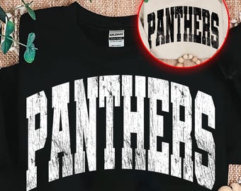 May include: Black sweatshirt with the word "PANTHERS" in distressed white lettering across the front. A smaller, tan sweatshirt with the same design is shown in a circular inset. The sweatshirt is a Gildan brand.