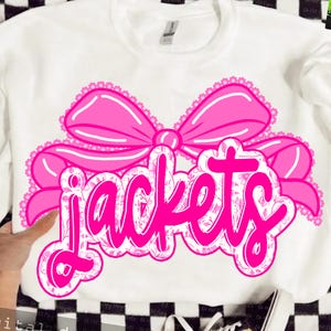 May include: White sweatshirt with a large pink bow and the word "Jackets" in a decorative pink font. The word "Jackets" is filled with a floral pattern. The sweatshirt is on a black and white checkered surface.
