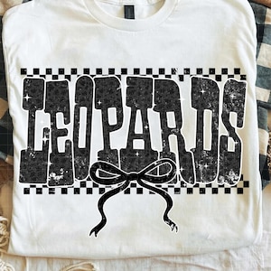 May include: White t-shirt with the word "LEOPARDS" in large, distressed black letters with leopard print fill. A black bow is centered below the text, and the design is framed by a black and white checkered border.