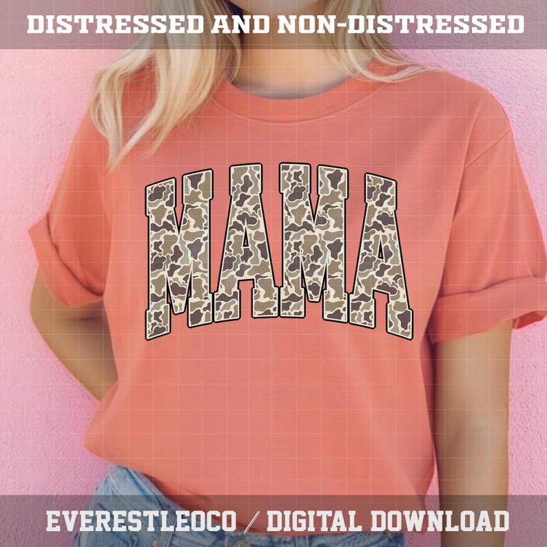 May include: A coral-colored sweatshirt with the word "MAMA" in large, block letters across the front. The letters are filled with a camouflage pattern in shades of brown and tan. The sleeves are rolled up. The text "DISTRESSED AND NON-DISTRESSED" is at the top.