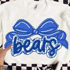 May include: White sweatshirt featuring a large blue bow and the word "bears" in a floral design. The bow has a scalloped edge. The word "bears" is in a script font with a blue floral pattern.