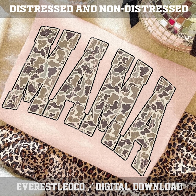 May include: A light pink t-shirt with the word "MAMA" in large, distressed camouflage letters. The shirt is displayed on a soft, textured surface with a leopard print fabric visible below. The text "DISTRESSED AND NON-DISTRESSED" is at the top.