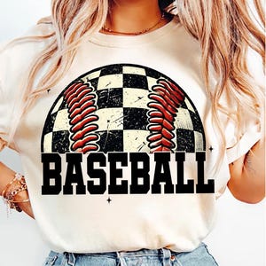 Pu&ograve; includere: Maglietta bianca con un grafico di baseball a scacchi bianco e nero e la parola "BASEBALL" in testo nero.