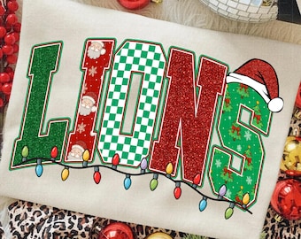 May include: Cream-colored sweatshirt with the word "LIONS" in a festive design. The letters are green, red, and checkered, with Santa Claus and Christmas tree accents. A string of colorful lights runs beneath the letters, creating a holiday theme.