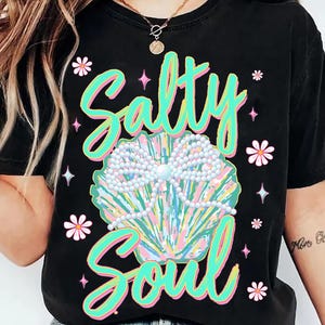 May include: Black t-shirt featuring a graphic of a seashell with pearls and the text "Salty Soul" in green and pink lettering.