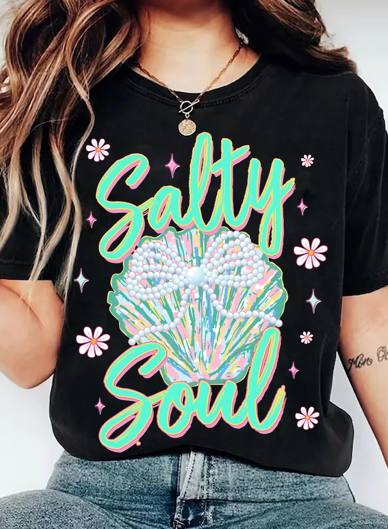 May include: Black t-shirt featuring a graphic of a seashell with pearls and the text "Salty Soul" in green and pink lettering.