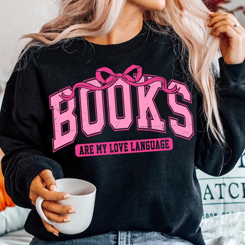 Pu&ograve; includere: Felpa nera con una grafica rosa che dice "BOOKS ARE MY LOVE LANGUAGE" con un fiocco rosa sopra la parola "BOOKS".