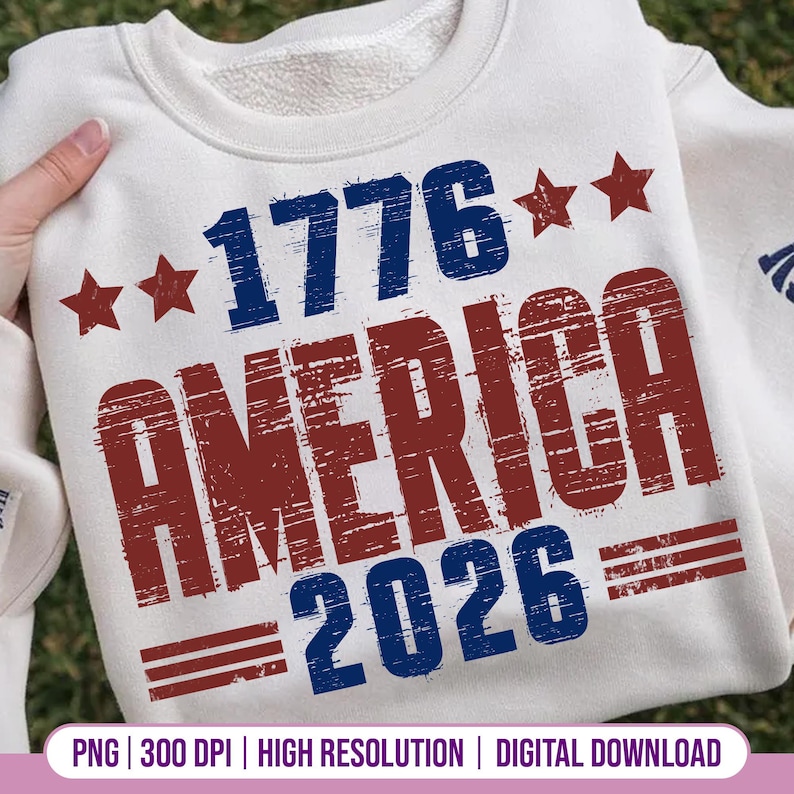 Op de afbeelding: Een witte sweatshirt met de tekst "1776 AMERICA 2026" in blauw en rood, met rode steraccenten. Het ontwerp heeft een distressed, vintage uitstraling. De sweatshirt wordt door een persoon vastgehouden.