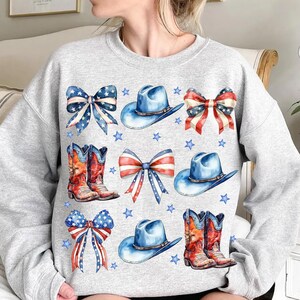 May include: A gray sweatshirt with a pattern of red, white, and blue cowboy hats, boots, and bows. The pattern is reminiscent of the American flag.
