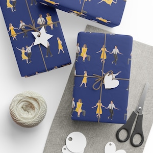May include: Gift wrap featuring a navy blue background with a repeating pattern of people in yellow dresses and suits. The wrapped gifts are tied with twine and adorned with star and heart-shaped tags. A spool of twine and scissors are also visible.
