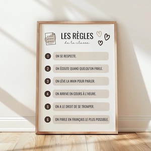 Puede incluir: Un cartel enmarcado con el texto "LES RÈGLES de la classe" y reglas numeradas en francés. Las reglas están en formato de lista con un fondo beige claro y un marco de madera. Incluye iconos de corazón y lista de verificación.