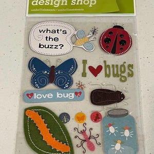 May include: A package of embellishments from the "Design Shop" collection, featuring insect-themed designs. Includes a ladybug, butterfly, and the phrase "I love bugs." The package contains 12 pieces.